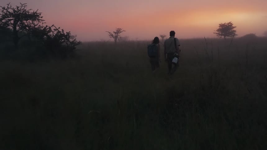 Two hikers walk across a misty field at sunrise