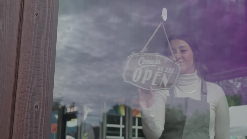 A woman inside a restaurant walks up to the sign to change it from closed to open