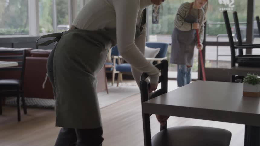 Staff members arrange chairs in a caf while tidying up the space