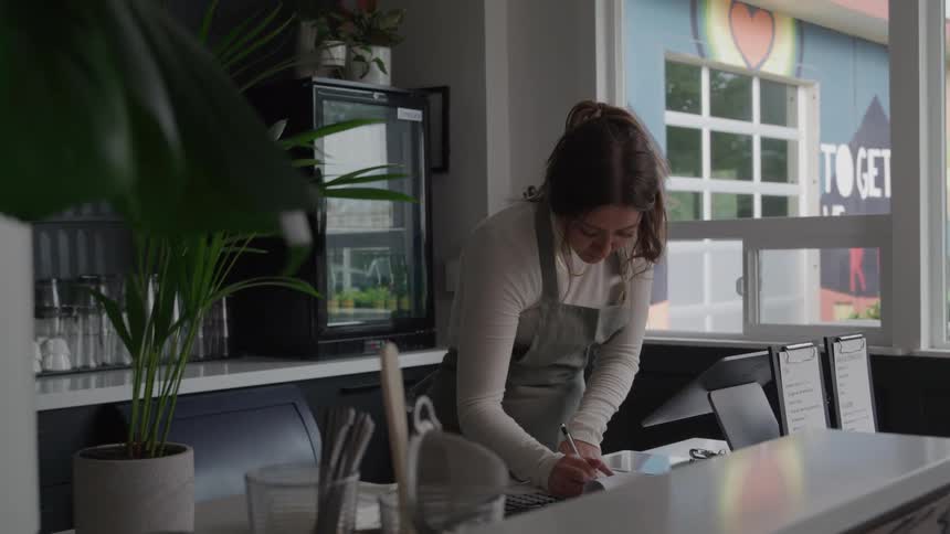 A woman in an apron operates a touchscreen register at a cafe