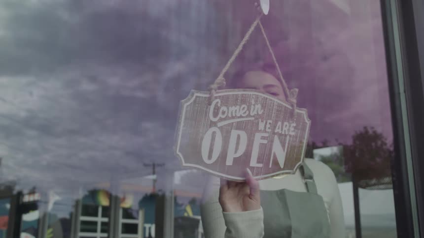 The video shows a person flipping a sign on a glass door the sign changes from reading sorry we are closed to come in we are open