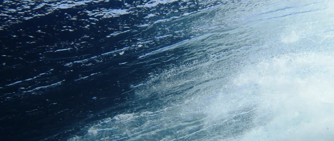 An underwater view shows waves on the surface of the ocean white foam can be seen as the waves crash down