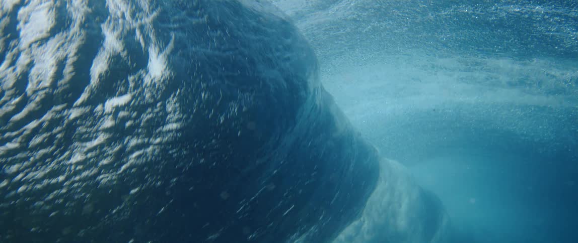 An underwater shot captures the powerful and turbulent motion of a large ocean wave as it rolls and breaks overhead