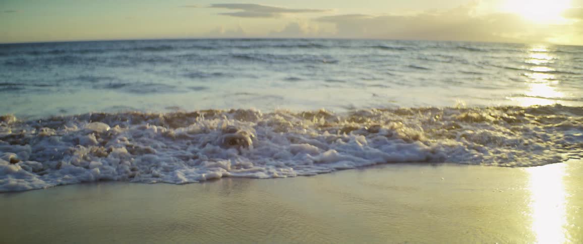 The sun setting at the beach with waves crashing against the shore creating foamy water