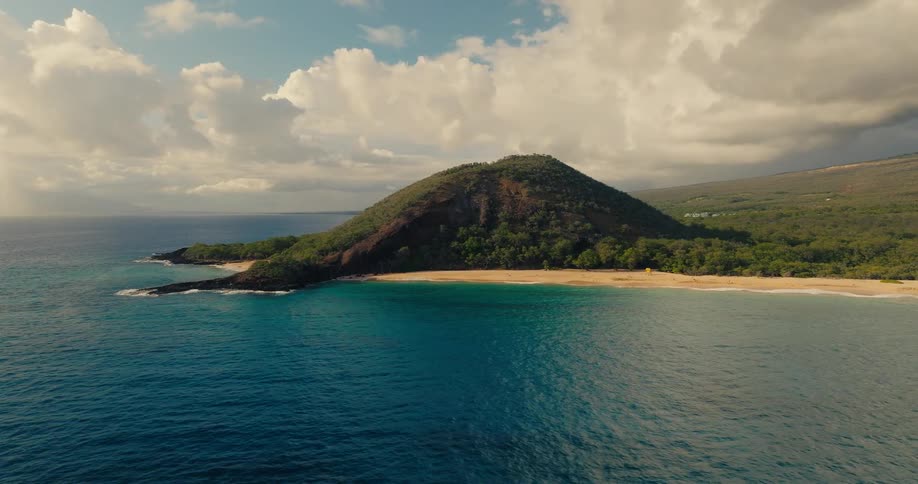 Hill covered with vegetation rises by a beach with blue waters