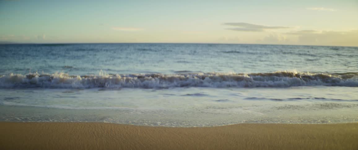 Wave gently breaks on the sand during sunset