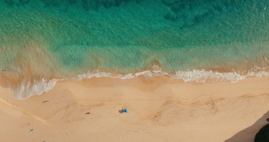 Aerial view looking down at people on the beach as waves roll into shore
