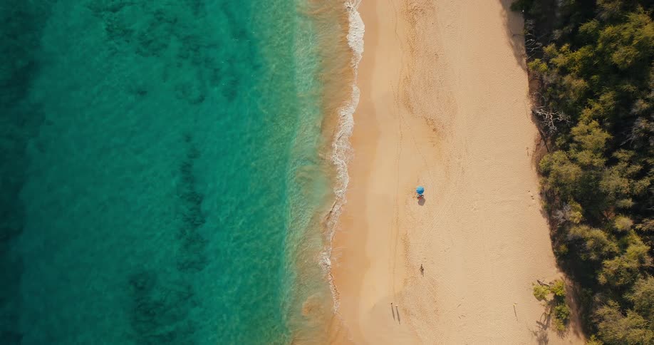 People walk along a beach while others are laying in the sun