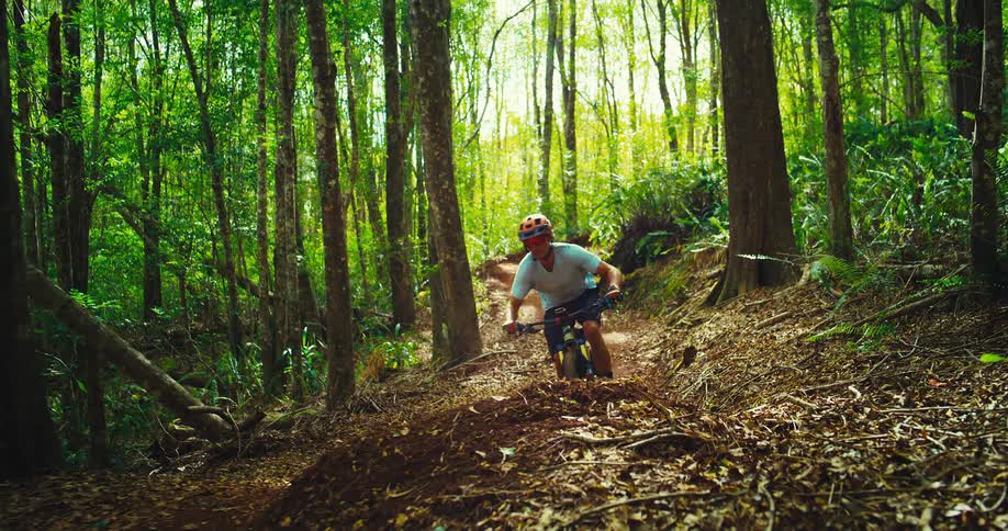 A man rides and jumps his mountain bike over a mound located in the forest