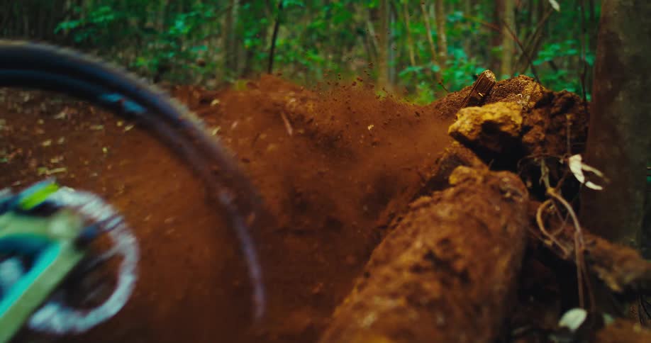 The video shows a mountain biker riding on a dirt trail the camera is close to the ground showing the bikes tires rolling over a large root and kicking up dirt