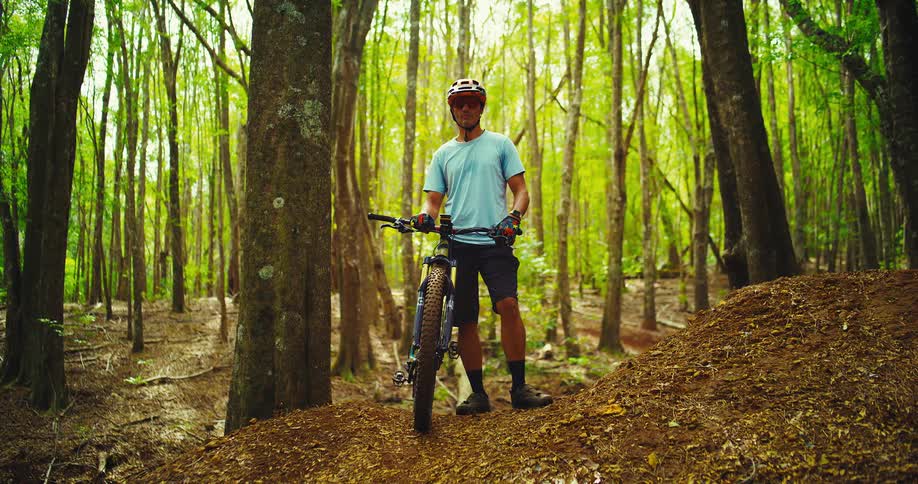 Man standing on a hill in the forest with his mountain bike