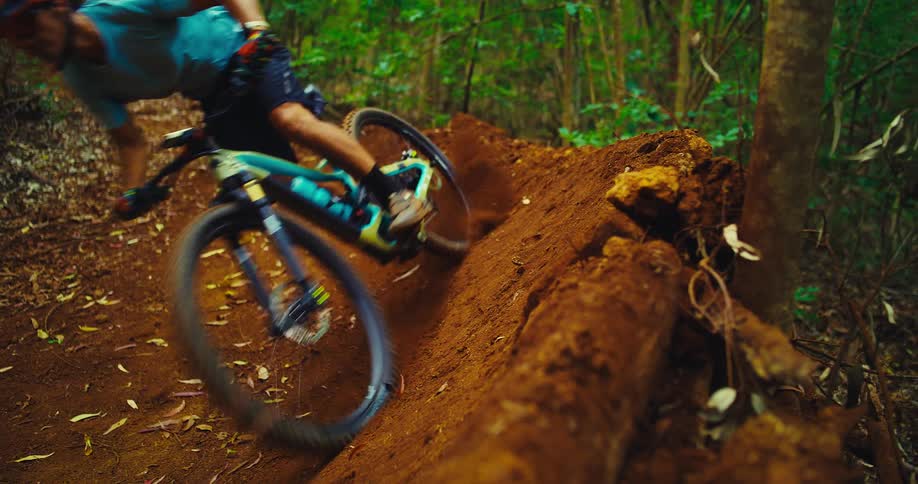 Mountain biker skidding on a dirt trail kicking up dust while maneuvering around an obstacle in the forest