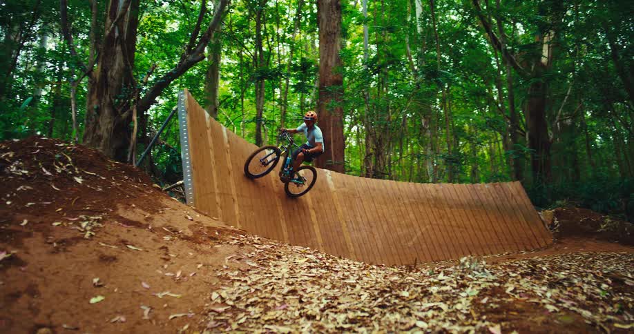 A cyclist rides on a wooden ramp in a forest setting