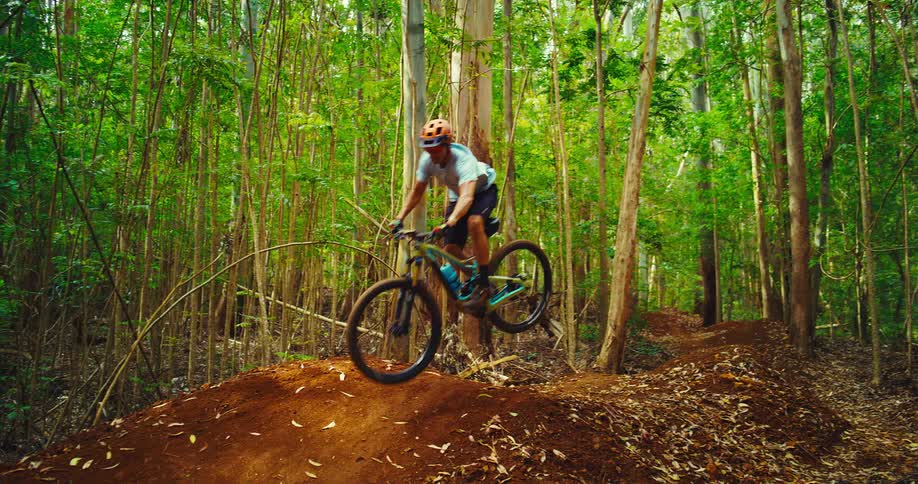 The video shows a mountain biker riding on a dirt trail through a forest the biker is seen riding up a ramp and becoming airborne for a brief moment