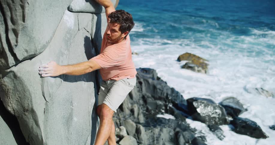 A man is climbing the side of a cliff at the waterfront
