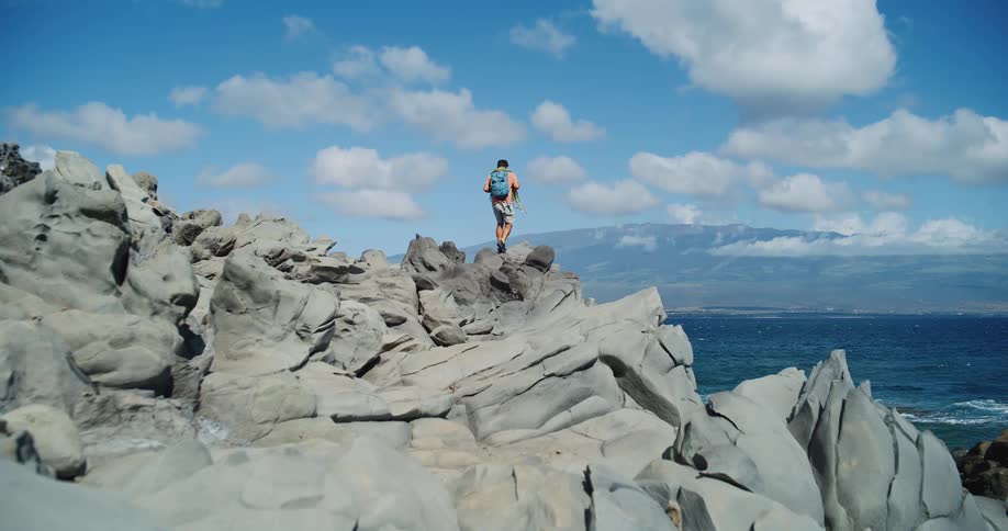 A man has hiked up a rocky cliff and is looking over the waterfront