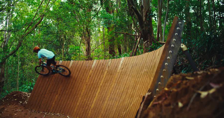 The man is riding his bike on a ramp in the woods