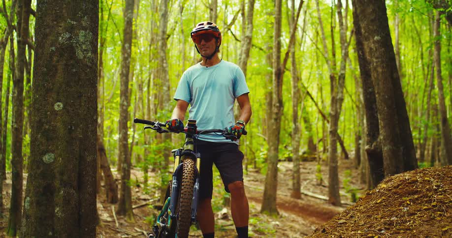 A man is standing next to his bike on a trail in the forest
