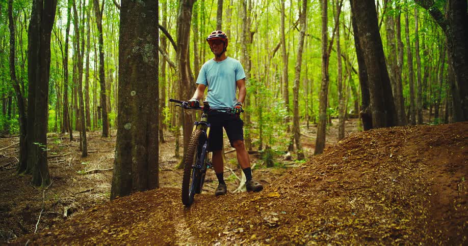 The man is standing by his bike in the woods