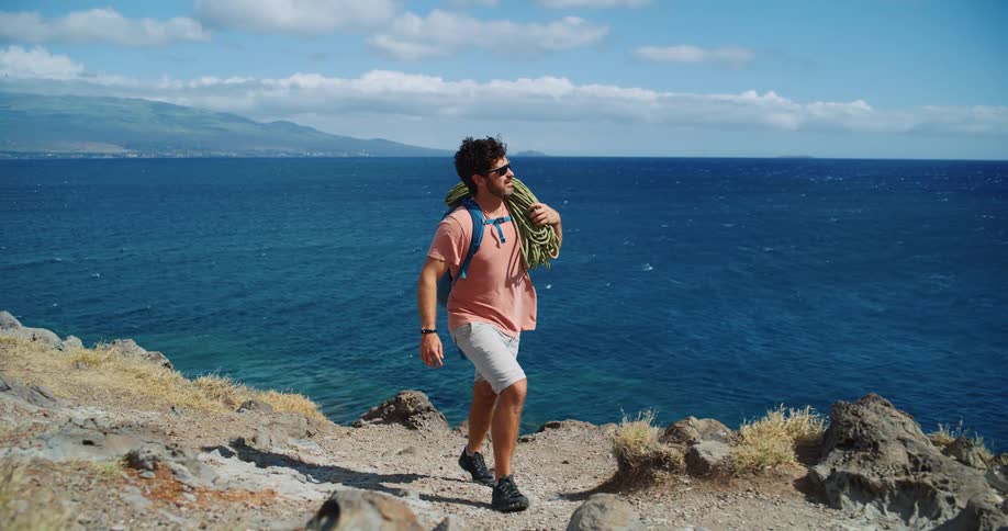 Man carrying rope on his shoulder walks along the edge of the coast