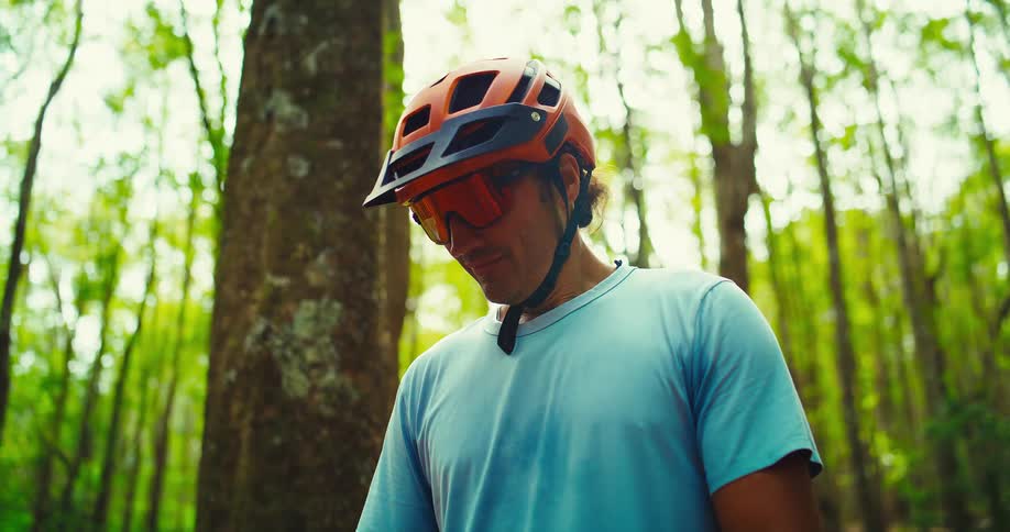 Cyclist wearing an orange helmet looks down in the forest