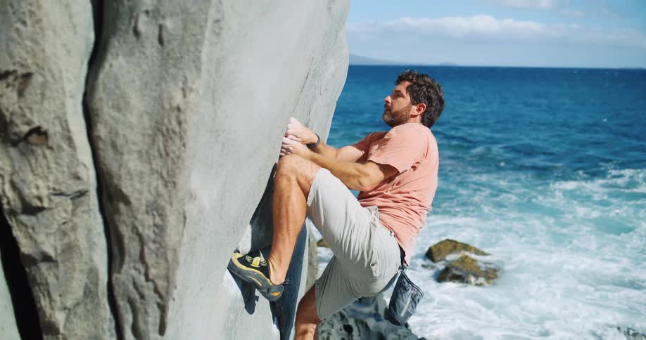 The man is rock climbing by the shore