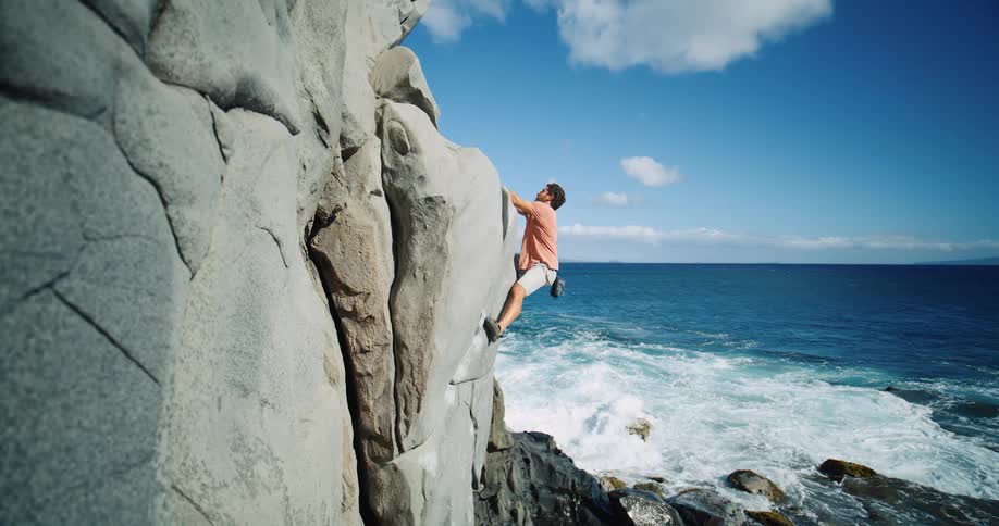 Man rockclimbing on side of rocks overlooking the coast