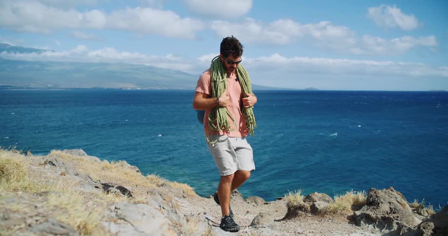 A man hikes along a rocky coastal cliff with the ocean in the background