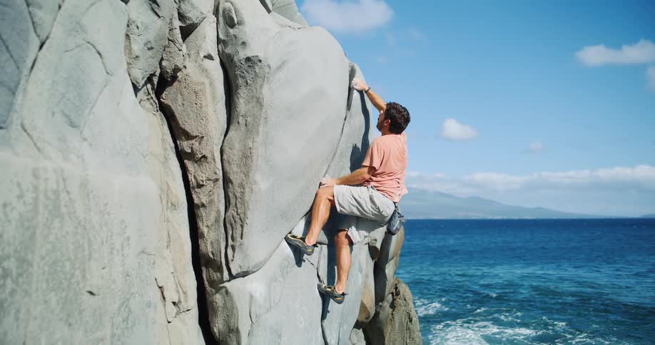 Man climbing a large rock by the sea on a sunny day