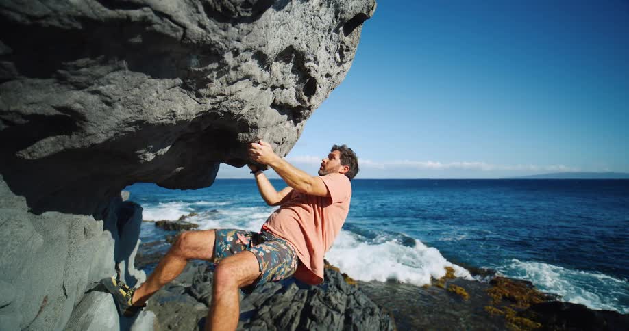 A man rock climbing a cliff beside the shore at midday