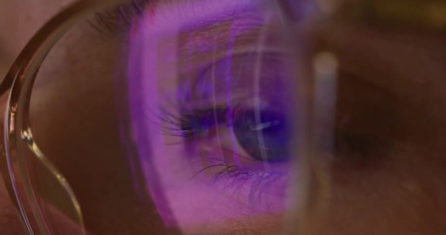 The video shows an extreme closeup of a persons eye and glasses the screen they are looking at is reflected in the lenses and it shows abstract colorful purple and blue patterns filmsupply is visible as a watermark on the video