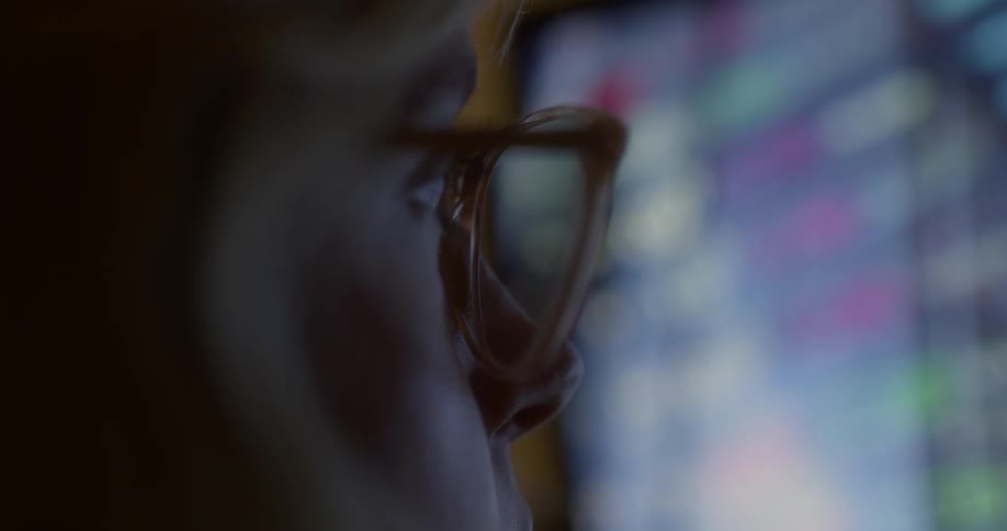 Person wearing glasses looks at a lit screen with colorful charts