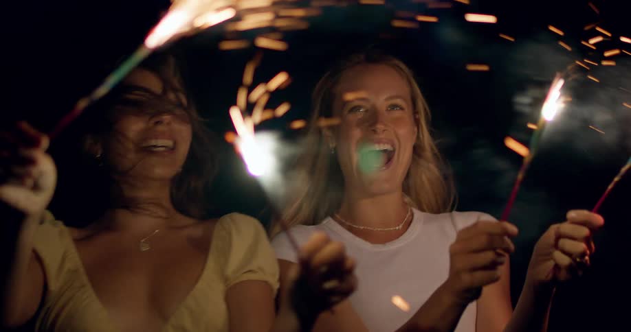 Two women celebrate joyfully with sparklers at night