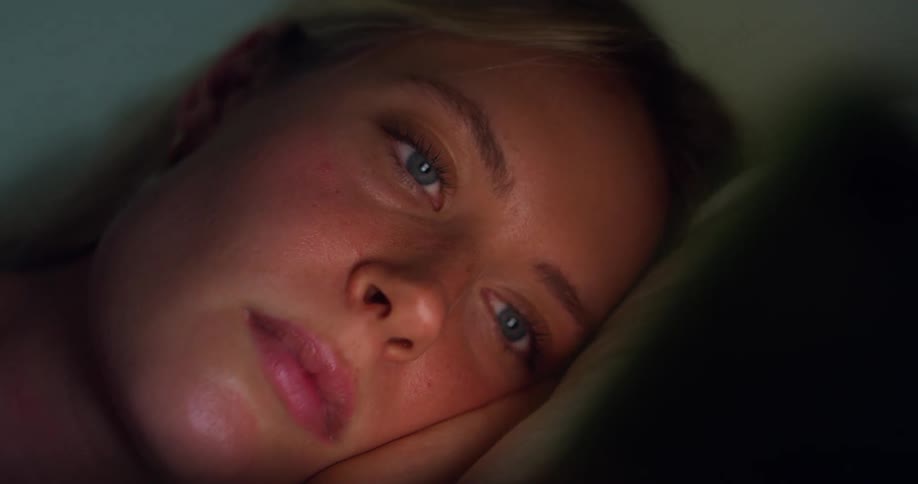 The face of a blonde woman with blue eyes lying down looking forward where there is a light illuminating her face