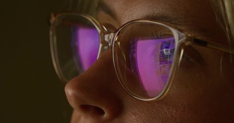 The video is a closeup of a persons face focusing on their glasses the reflection on the glasses shows a screen with colors and shapes moving across it