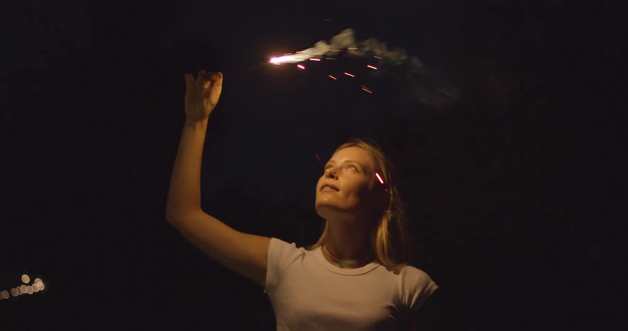 The woman raises the lit sparkler at night