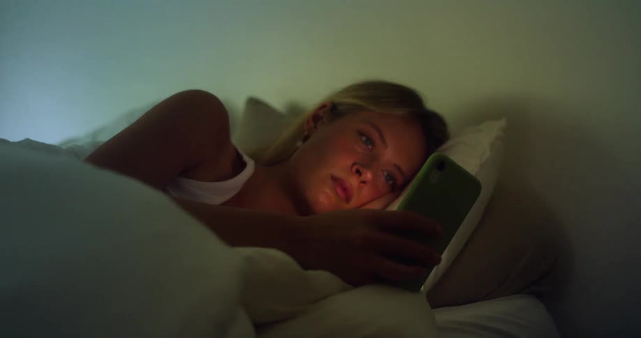A woman lies in bed looking at her phone in a bedroom