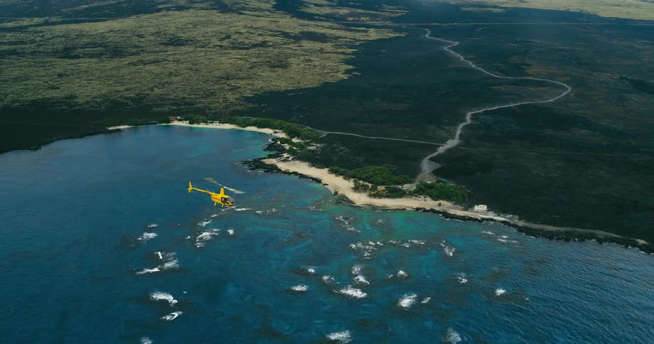 A yellow helicopter flies above the body of water next to a stretch of coastal plain