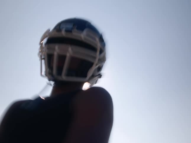 American football player putting on gloves with the bright sun behind creating a silhouette effect