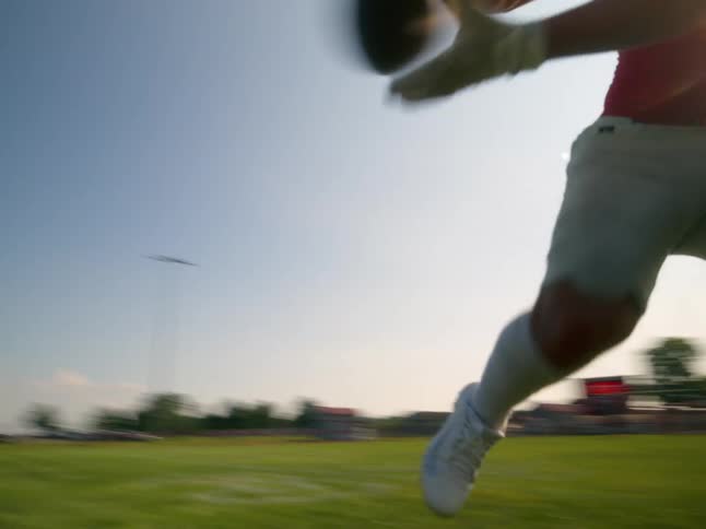 A lowangle shot of a football player in a red jersey and white pants running and expertly catching a football on a grassy field