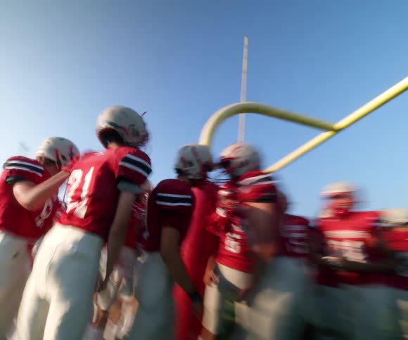 Football players huddle under the goalpost at golden hour
