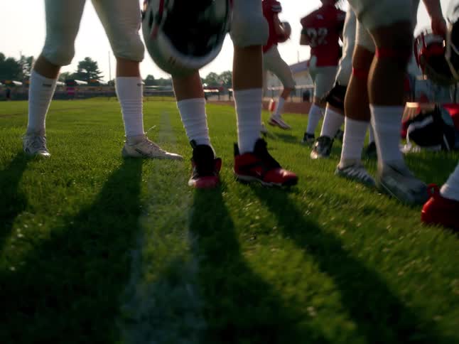 A football player puts his helmet on the grass as the team walks