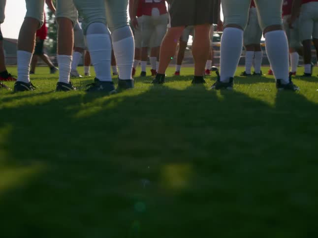 Football players stand together during practice on a grassy field