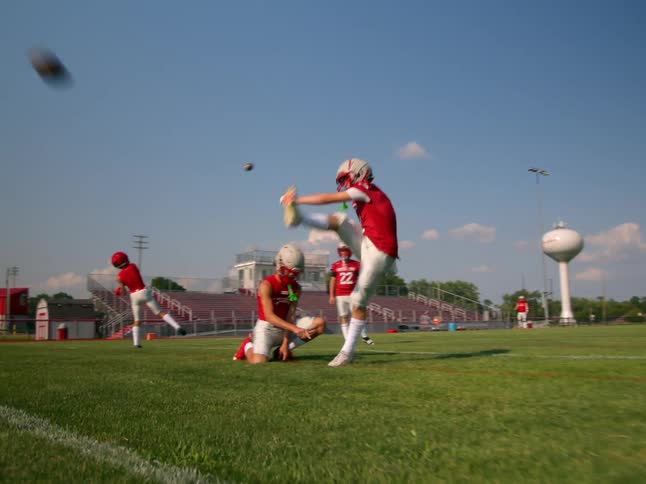 A football player in a white and red uniform kicks a football off the tee other players are standing nearby