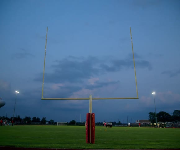 American football goalpost lit at dusk on a grassy field