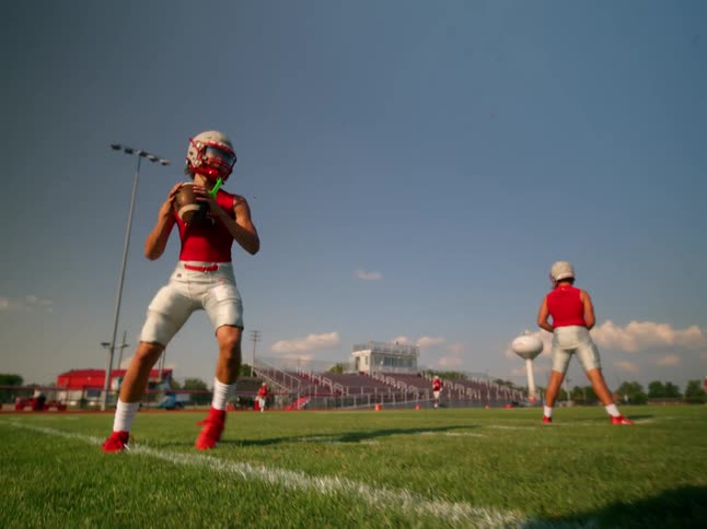 A man is receiving an american football on a green grass field and then throwing it away