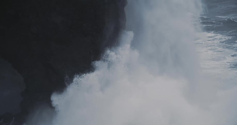 A huge wave crashes against a rocky cliffside by the ocean