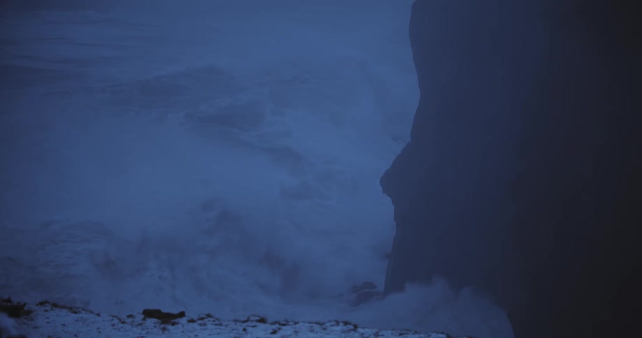 A massive ocean wave crashes against a towering cliff