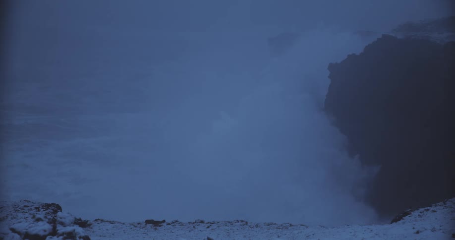 Ocean waves violently crashing against a rocky shore creating splashes at sunset