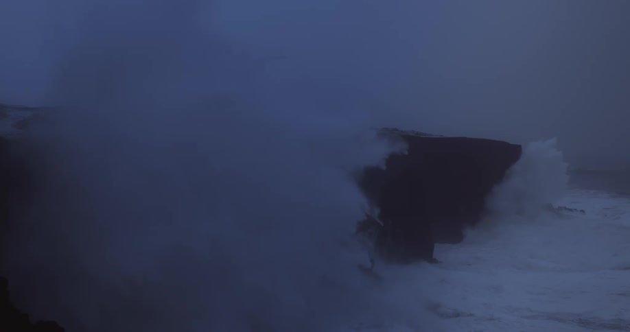 A stormy wave strikes dark cliffs with a lighthouse in the distance